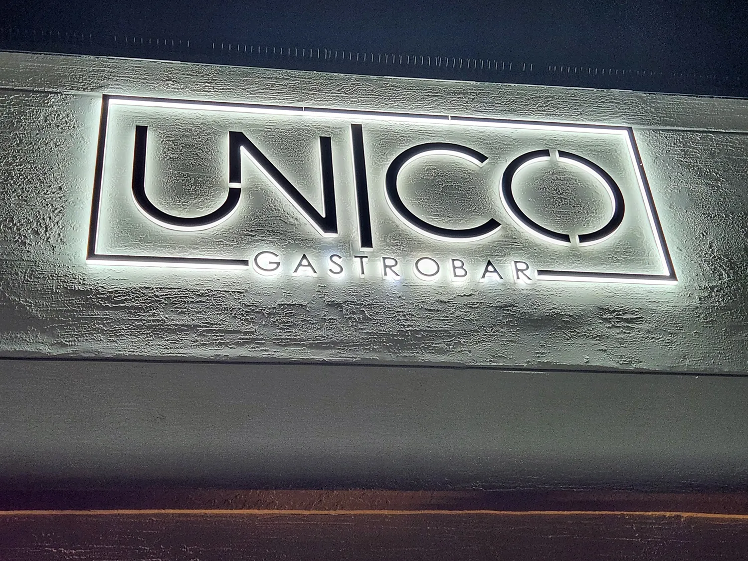 Close-up of the illuminated UNICO Gastrobar sign glowing against a dark facade