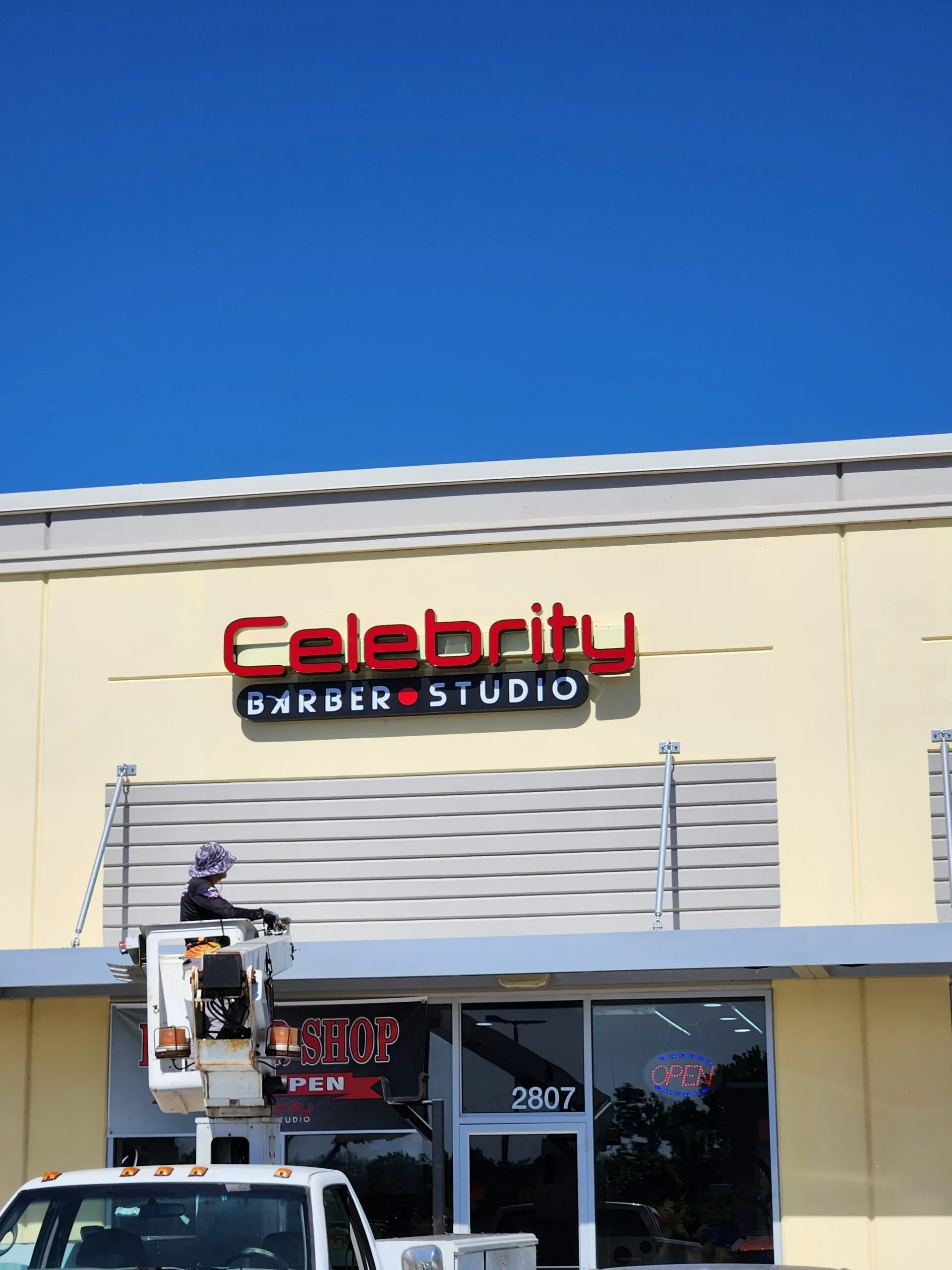 Installer on a bucket truck mounting the Celebrity Barber Studio sign on a storefront