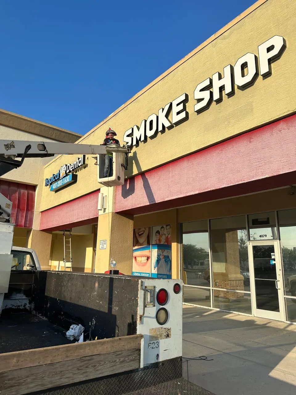 Installer on a bucket truck fitting white SMOKE SHOP letters to a shopping-center facade