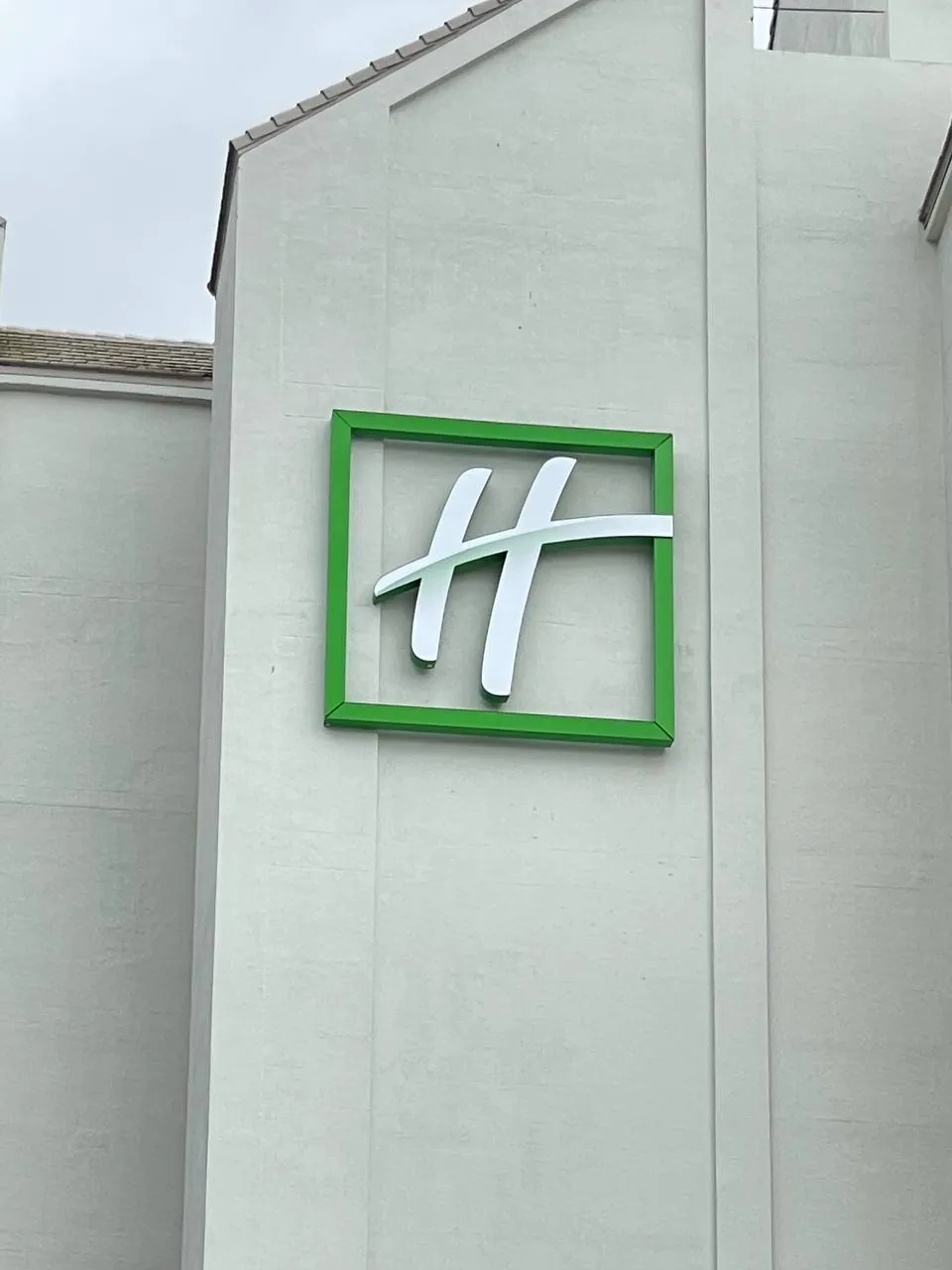 Green-framed H logo sign with white dimensional lettering on a hotel wall by day