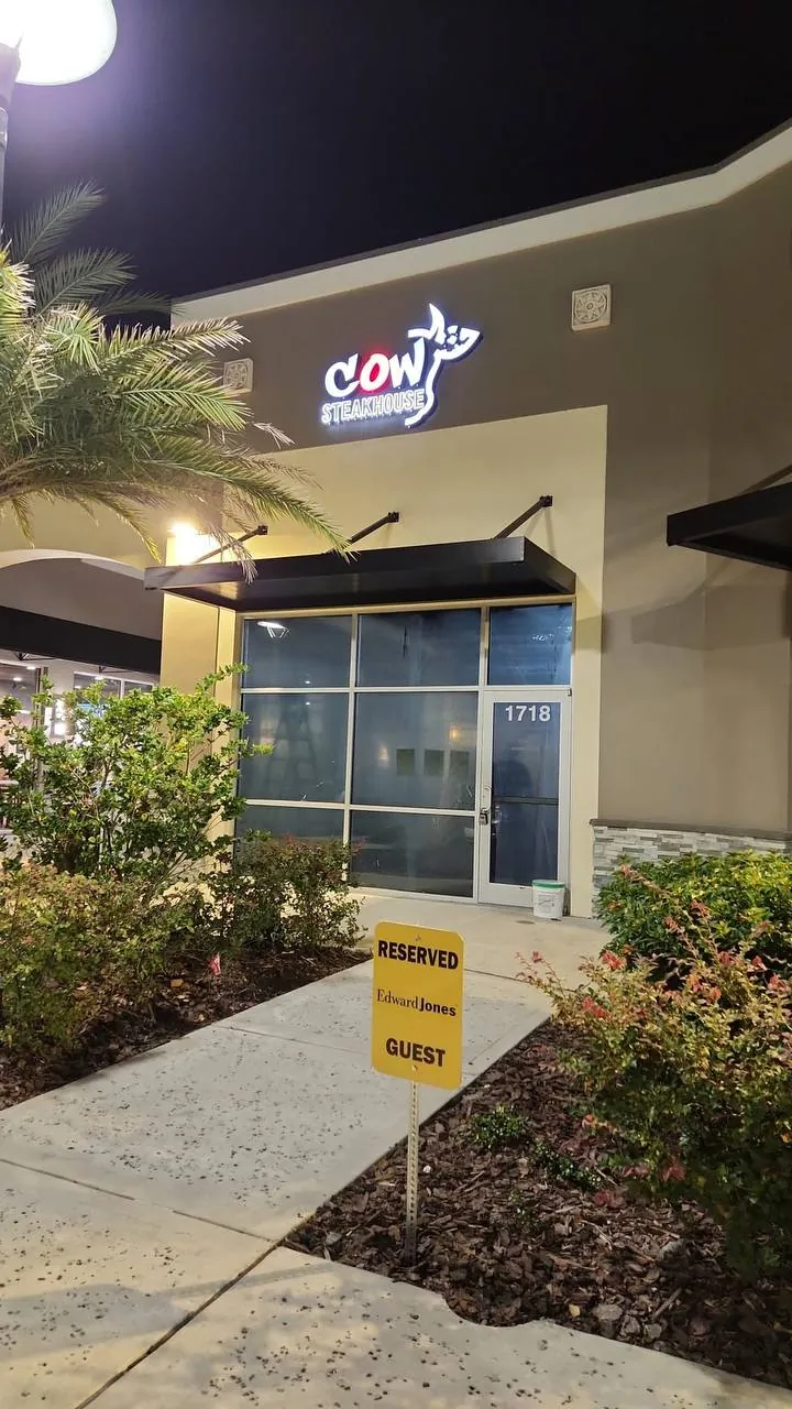 Cow Steakhouse illuminated logo sign above a restaurant entrance at night