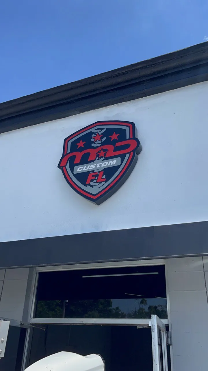 MAD Custom FL red and black shield logo sign on a white facade by day