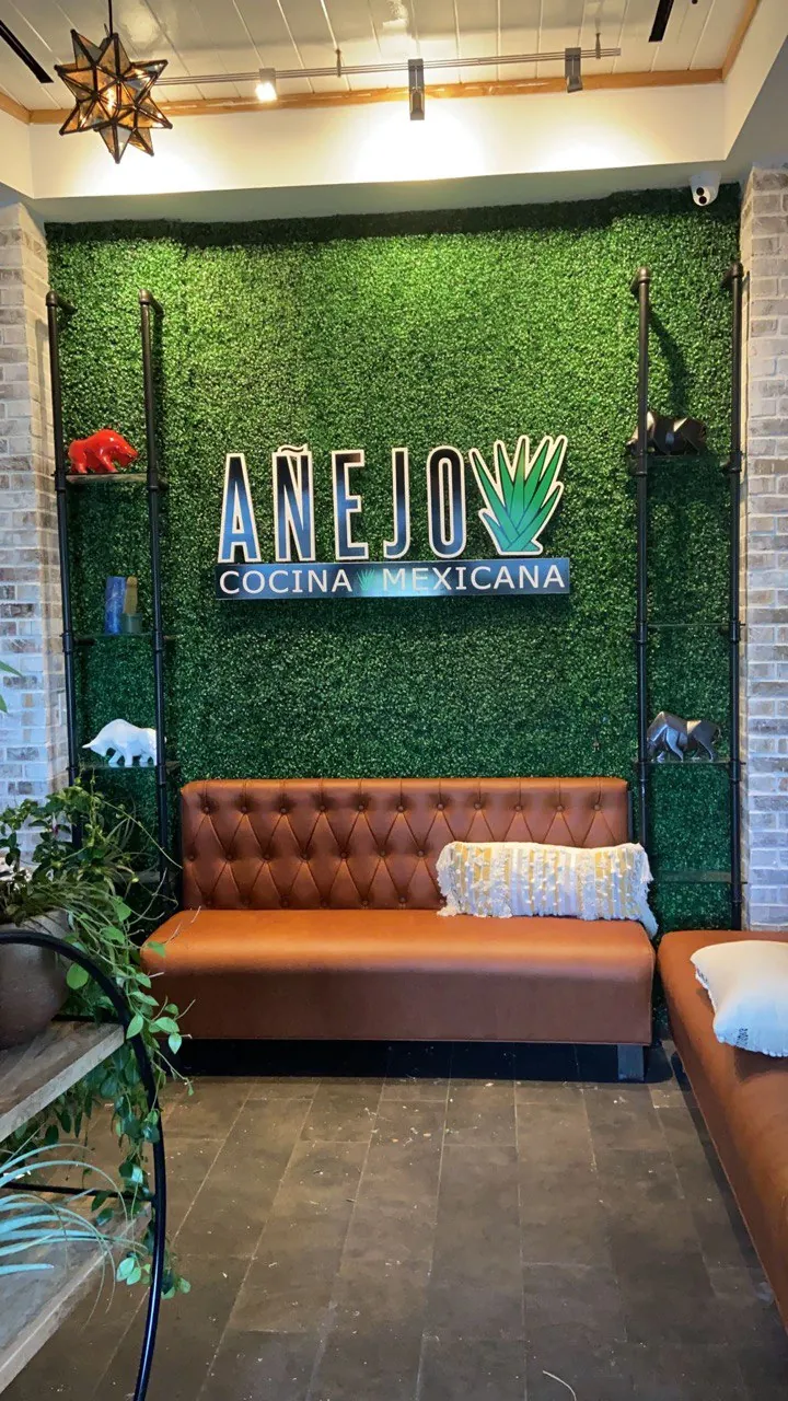 Illuminated Añejo logo on a boxwood wall above restaurant booths
