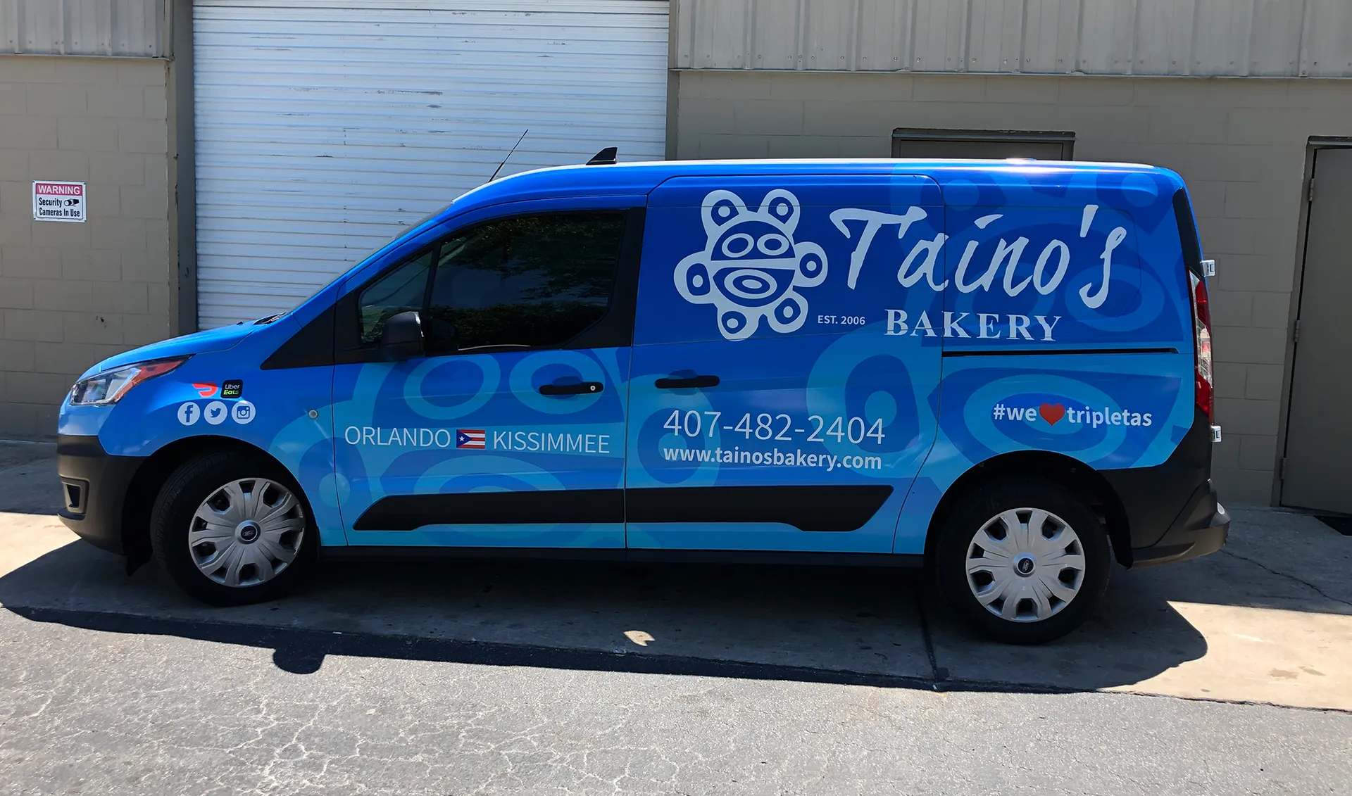 Blue Taíno's Bakery cargo van with a full printed wrap parked outside a warehouse